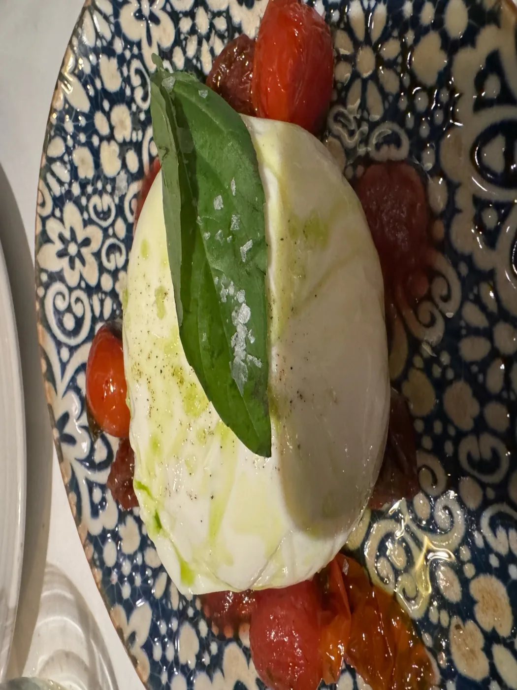 Burrata with roasted tomatoes, basil and olive oil on a patterned plate